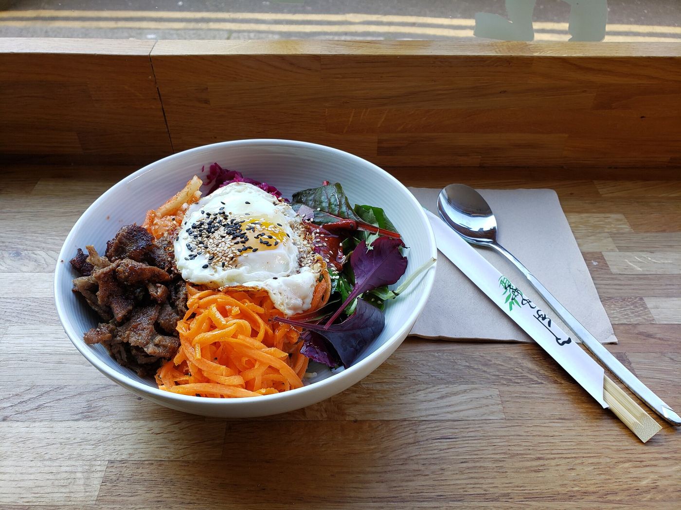A bowl of beef bibimbap with vegetables and a fried egg