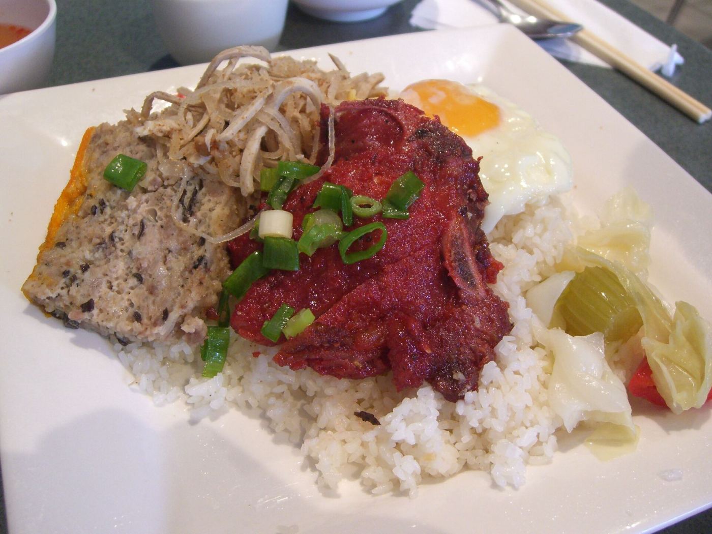 A plate of com tam with grilled pork, egg, and pickled vegetables