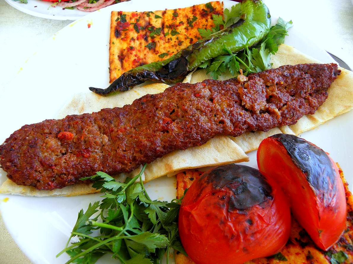 Adana kebab served on a skewer with grilled vegetables