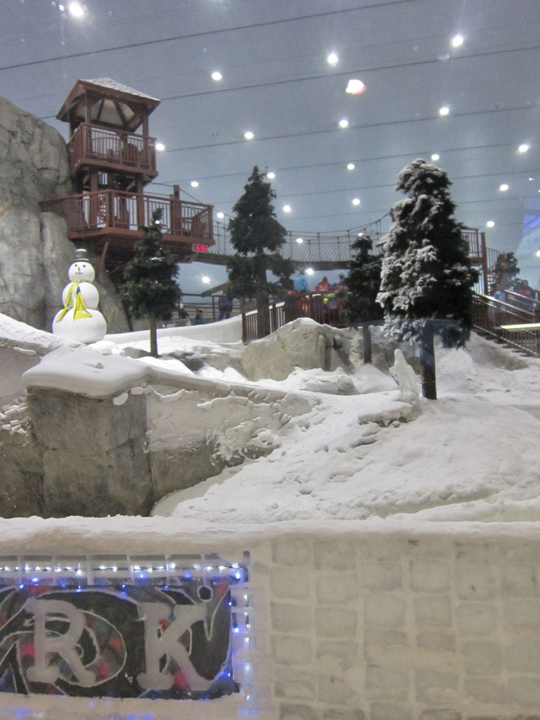 Snow-covered slope with pine trees and a snowman inside Ski Dubai indoor snow park