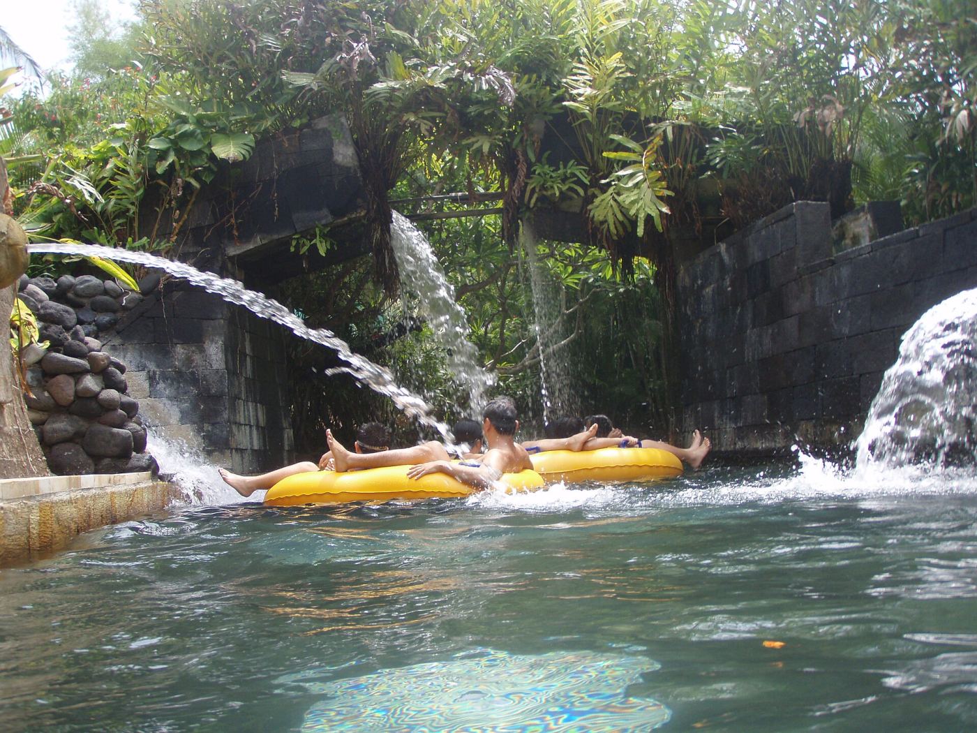 People floating on inflatable tubes down a lazy river surrounded by tropical plants at Waterbom Bali