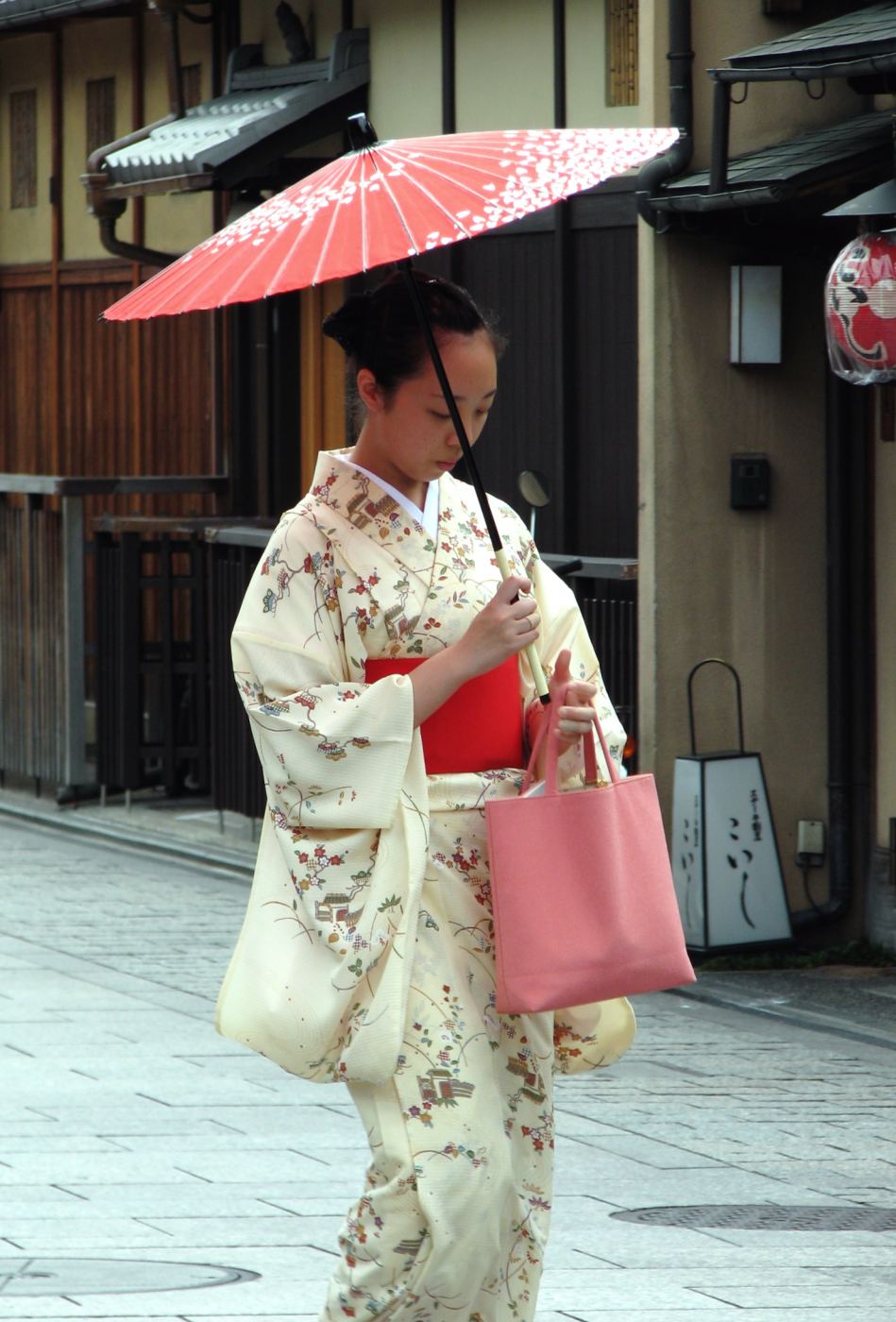 A woman in a traditional cream kimono holding a red parasol on a street in Gion, Kyoto