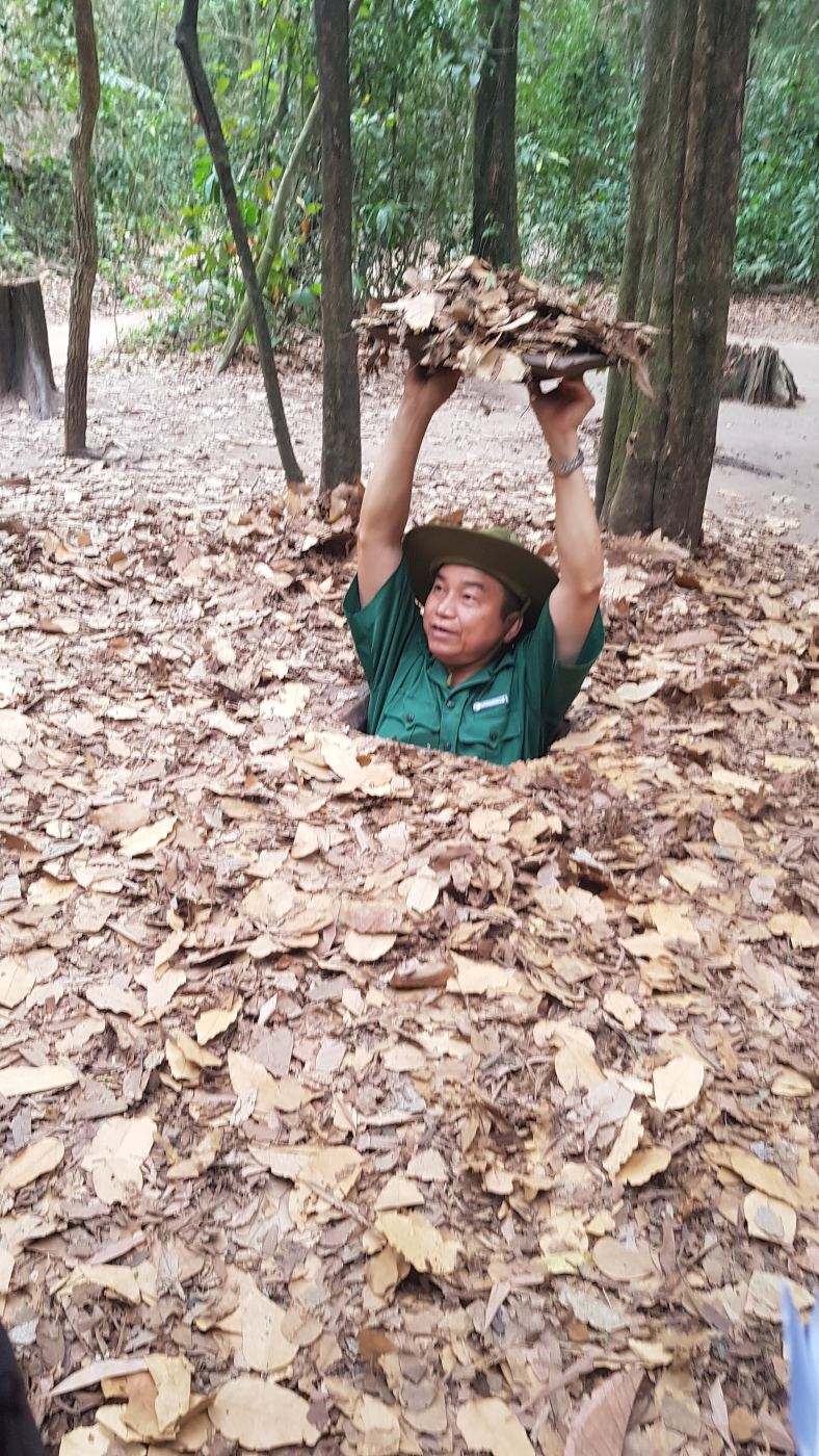A guide demonstrating a camouflaged entrance to the Cu Chi Tunnels in Vietnam