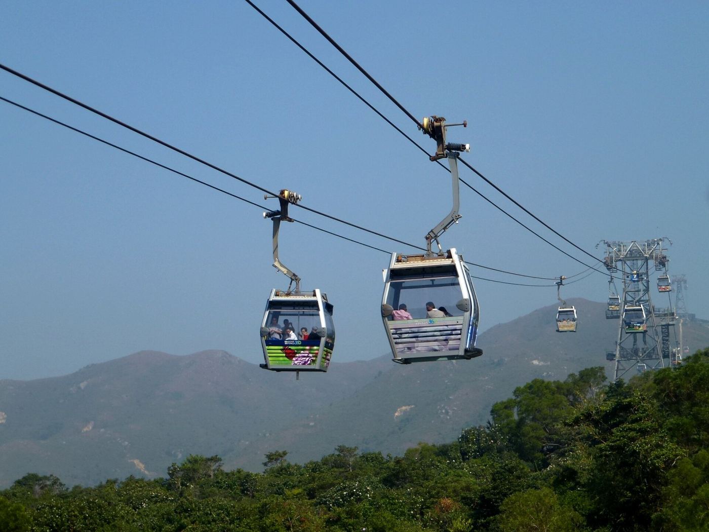 Cable cars traveling over green hills on Lantau Island toward Ngong Ping village