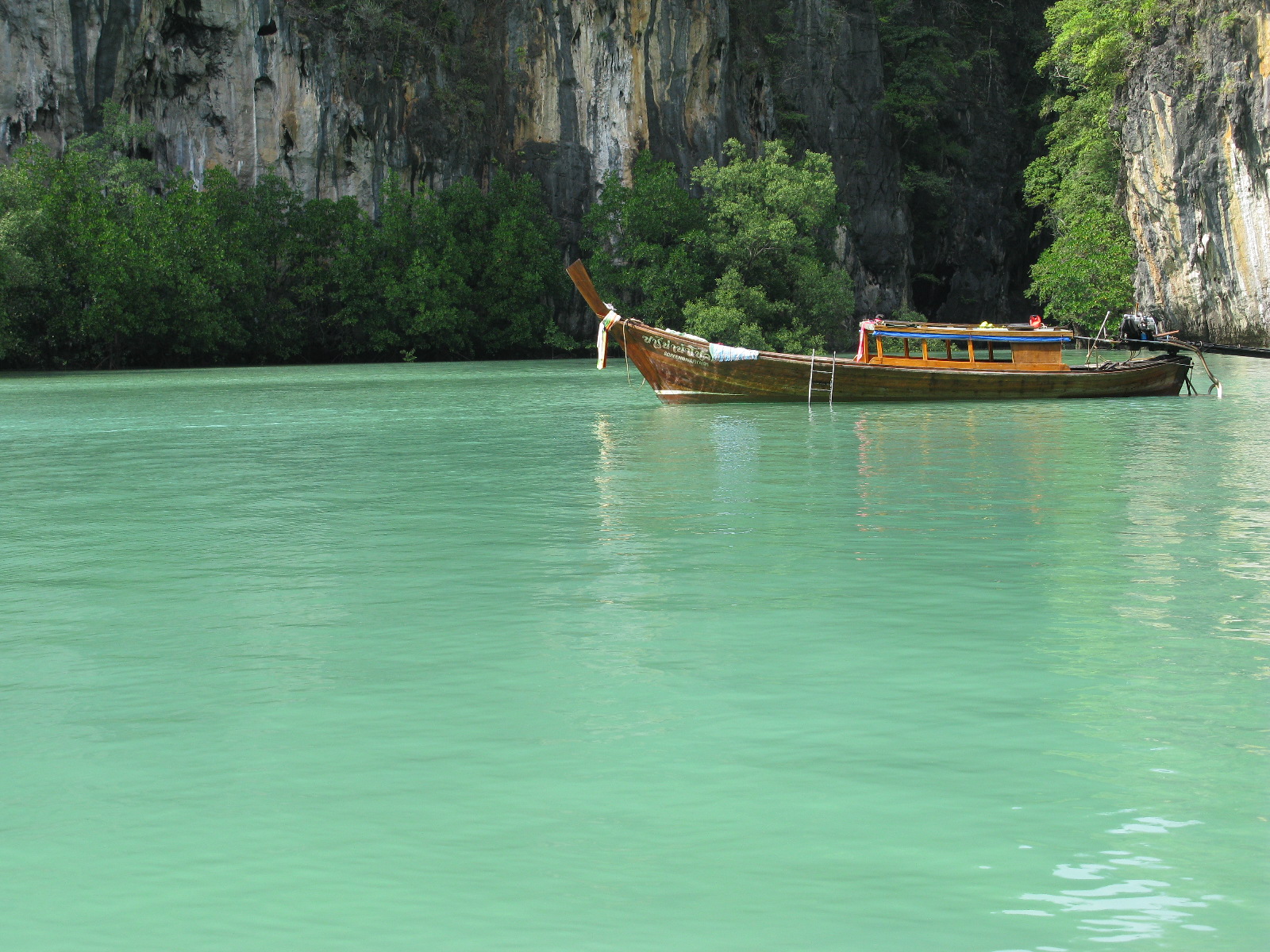 A traditional wooden longtail boat anchored in clear turquoise water near limestone cliffs in Thailand
