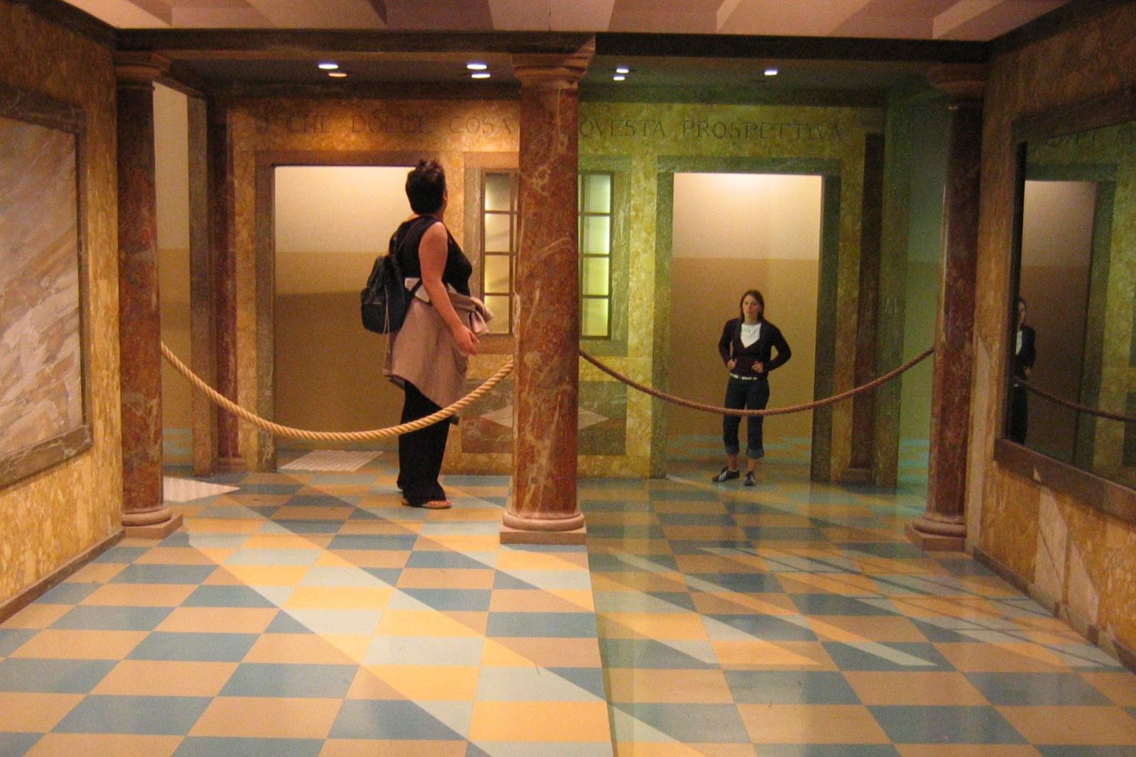 Visitors standing in an Ames room, an optical illusion exhibit that distorts perceived size and perspective