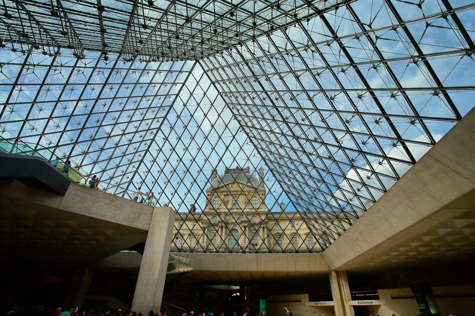 The glass pyramid entrance of the Louvre Museum viewed from inside, framing the historic palace behind it