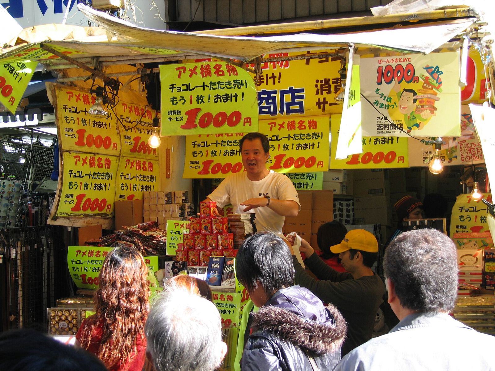 A vendor selling chocolate and snacks at a busy stall in Ameyoko market, Ueno, Tokyo, with crowds of customers