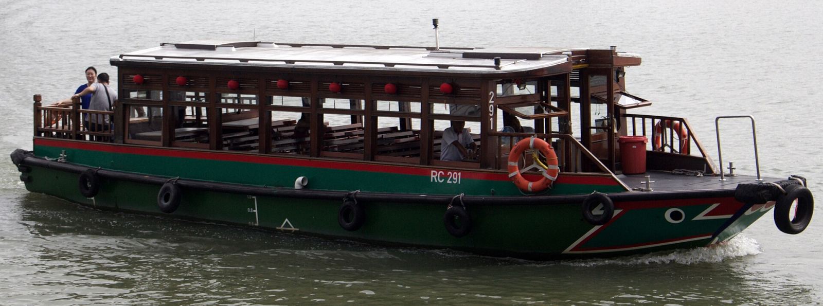 A traditional green and red Singapore River bumboat used for river cruises, photographed on the water