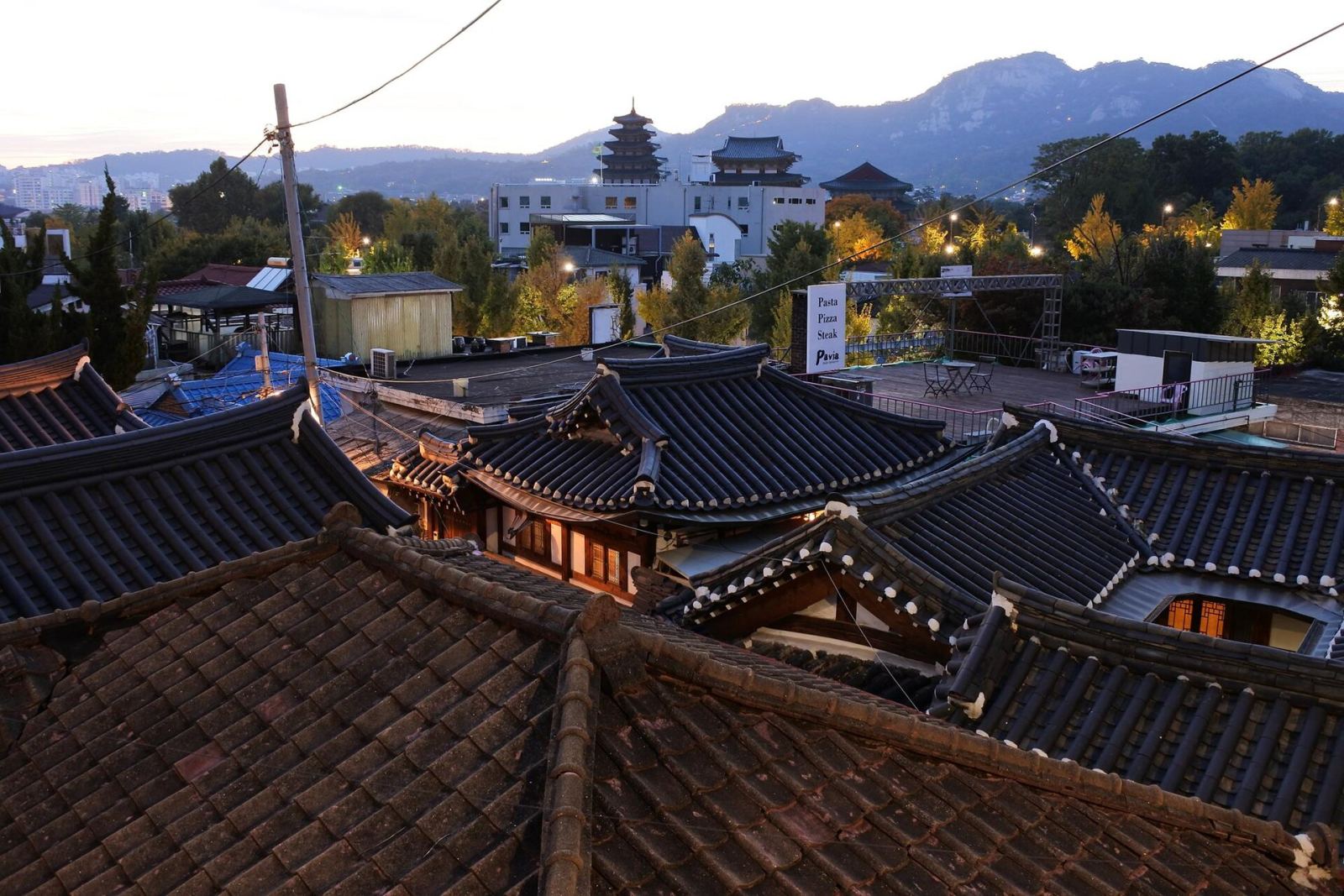Hanok rooftops in Bukchon Village, Seoul, at dusk with the city skyline behind